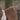 A close up image of a hand holding a chestnut brown knitted headband outside.